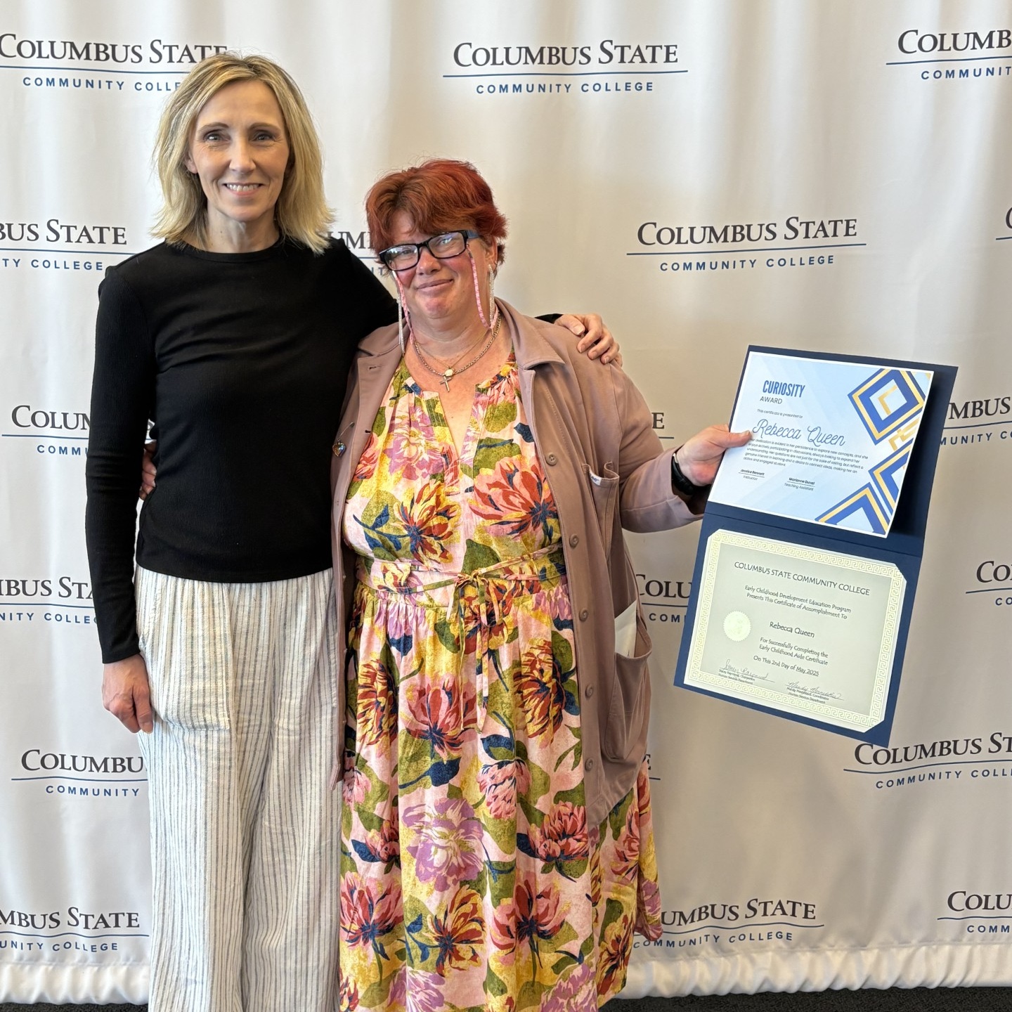 Two people smiling with one holding a certificate